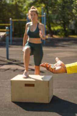 Spor sahasında spor yapan bir kadının arka planında kronometresi olan bir antrenörün eli. Sağlıklı yaşam tarzı