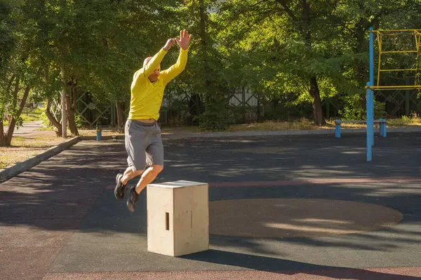 Man jumps over a wooden box while exercising at an outdoor sports ground. Healthy lifestyle
