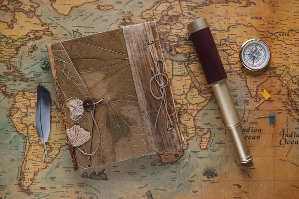 Spyglass, a compass, a vintage leather book and a bird\'s feather - a symbol of travelers lie on an old map. View from above