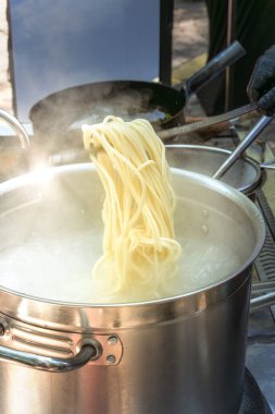 Aşçı, bir sokak kafesinde Asya yemekleri pişirmek için tavadaki haşlanmış erişteleri çıkarır. Fast food