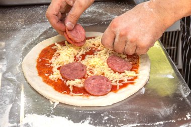 Şef sosisi peynirin üstüne, domatesliyi de pizza hamurunun üzerine serer. Yakın plan.