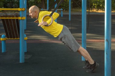 Güneşli bir günde spor sahasında jimnastik yüzükleriyle antrenman yapan bir adam. Sağlıklı yaşam tarzı