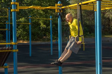 Güneşli bir günde spor sahasında jimnastik yüzükleriyle antrenman yapan bir adam. Sağlıklı yaşam tarzı