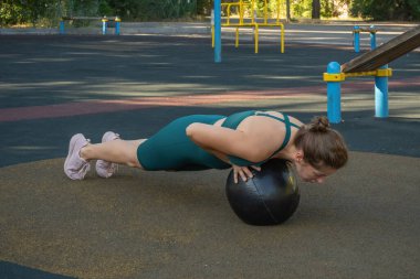 Beyaz bir kadın sokak sporları sahasında tıp topuyla şınav çekiyor. Sağlıklı yaşam tarzı