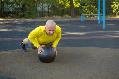 Avrupalı bir adam, sokak sporları sahasında bir tıp topuyla şınav çekiyor. Sağlıklı yaşam tarzı