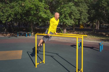 Adam güneşli bir yaz gününde sokak sporları alanında paralel barlarda egzersiz yapıyor. Sağlıklı yaşam tarzı