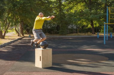 Adam açık hava spor sahasında egzersiz yaparken tahta bir kutunun üzerinden atlıyor. Sağlıklı yaşam tarzı