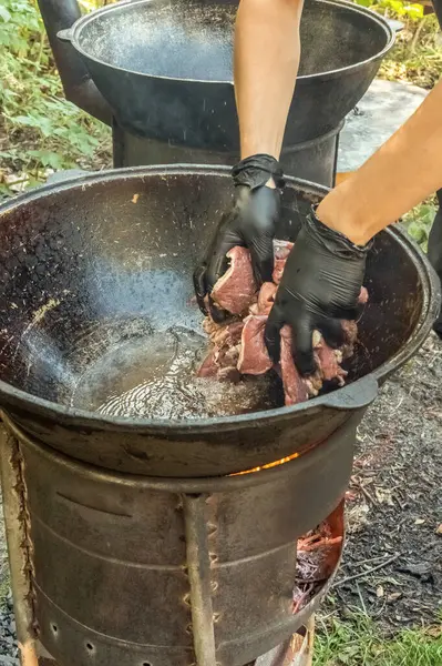 厨师把切碎的肉放在室外烧木柴的炉子上的铸铁大锅里 街头食品 — 图库照片