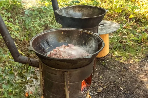肉の部分は 屋外の木製燃焼ストーブに鋳鉄製のカルドロンで熱い油で揚げられています ストリートフード — ストック写真