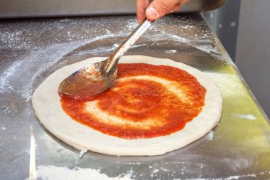 Şef pizza hamurunun üzerine domates tabanı yaymak için kaşık kullanıyor. Yakın plan.