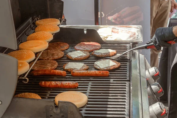 Process of cooking meat for burgers and cheeseburgers, sausages for hot dogs, buns on a grill with burning coals. Street food