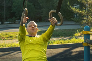 Adam güneşli bir günde sokak sporları sahasında jimnastik halkalarıyla egzersiz yapıyor. Sağlıklı bir yaşam tarzı. Yakın plan.