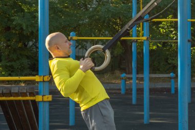 Adam güneşli bir günde sokak sporları sahasında jimnastik halkalarıyla egzersiz yapıyor. Sağlıklı yaşam tarzı