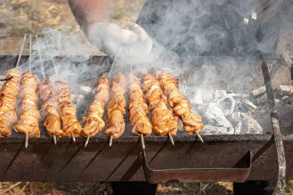 Chef\'s hand turns over a kebab with pieces of meat while cooking on a charcoal grill for a family party. Grill, barbecue, picnic