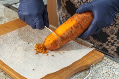 Kadın mutfak tahtasının üzerinden bıçakla taze havuç soyuyor. Yakın plan.