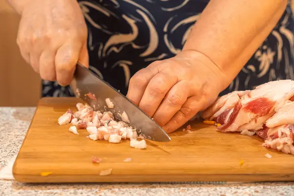 Woman cuts meat into small pieces on a kitchen wooden board to prepare minced meat. Homemade food