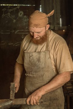 Bandanalı bir tamirci, bir sokak atölyesinde çekiçle metal bir boruyu düzleştiriyor. Yakın plan.