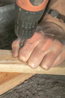 Usta, yerdeki tahta blokları tutturmak için elektrikli kablosuz tornavida kullanıyor. Yakın plan.