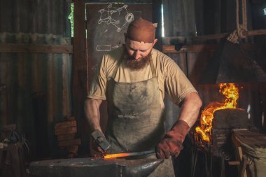 Demirci, kırsal bir demir ocağında bir örsün üzerinde kızgın metal bir parça dövüyor. Geleneksel el sanatları