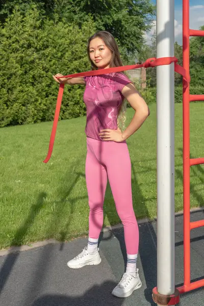 stock image Asian girl exercising with a rubber expander on a street sports ground. Sport and Recreation.