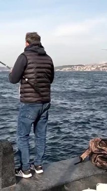 İstanbul, Trkiye - 29 Nisan 2022. Balıkçı boğazın kıyısında bir oltayla balık yakalar.