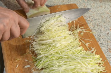 Bir aşçı sebze salatası hazırlamak için tahta kesme tahtasının üzerinde bıçakla ince ince beyaz lahana dilimler. Yakın plan. Vejetaryenlik ve çiğ gıda diyeti kavramı.