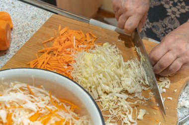 Aşçı havuçlu sebze salatası hazırlamak için tahta kesme tahtasının üzerinde bıçakla ince ince beyaz lahana keser. Vejetaryenlik ve çiğ gıda diyeti kavramı.