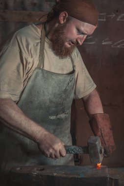 Demirci, kırsal bir demir ocağında bir örsün üzerinde kızgın metal bir parça dövüyor. Geleneksel el sanatları