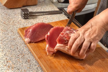 Aşçı bir parça çiğ eti biftek ya da pirzola olarak bıçakla keser. Yakın plan.