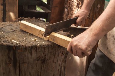 Adamın eli metal bir satırla tahta çıtayı kesiyor. Yakın plan.