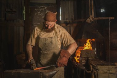 Demirci, kırsal bir demir ocağında bir örsün üzerinde kızgın metal bir parça dövüyor. Geleneksel el sanatları