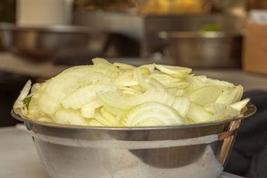 Soğanlar, mutfak metal aletlerinin arka planına karşı paslanmaz çelik bir kasede yarım halkalar halinde kesilmiş. Yakın plan.