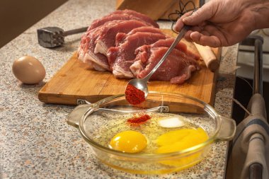 Aşçı, arkaplanda domuz filetosu ve et tokmağı ile irtibat kurmak için kırık yumurtalı bir tabağa kırmızı biber ekler. Yakın plan.