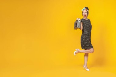 Pin tarzı giyinmiş, parlak sarı arka planda geçmişe dönük kayıt cihazı olan seksi Asyalı kız. İzole edilmiş. Boşluğu kopyala