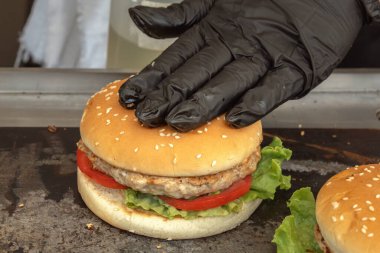 Şef, kızarmış susamlı ekmeği hazır hamburgerin üzerine koyar. Sokak yemeği. Yakın plan.