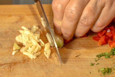 Bir aşçı ahşap kesme tahtasındaki taze sarımsağı ince şeritlere ayırır. Yakın plan.