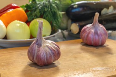 Ahşap mutfak tahtasındaki sarımsak başı diğer sebze ve otların arka planına karşı..