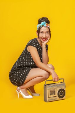 Pin tarzı giyinmiş güzel bir Asyalı kız. Parlak sarı arka planda geçmişe dönük kayıt cihazı var. İzole edilmiş.
