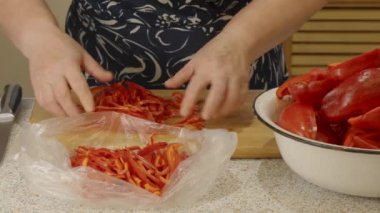 Bir kadının elleri, dilimlenmiş kırmızı dolma biberleri dondurucuya koyuyor.