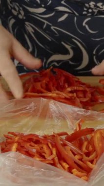 Bir kadının elleri, dilimlenmiş kırmızı dolma biberleri dondurucuya koyuyor.