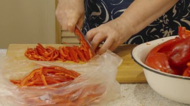 Kadın kırmızı dolma biberi dilimlemek için bıçak kullanıyor ve dondurucuya koyuyor.