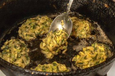 Şef, krep yapmak için eski dökme demir tavada haşlanmış yağın içine otlarla dolu kabak kaşıkları koyuyor. Yakın plan.