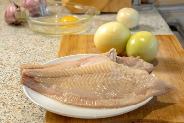 Soğan kafalarının arka planına ve cam tabakta kırılmış tavuk yumurtasına karşı hazırlamak için temizlenmiş taze balık leşleri. Yakın plan.