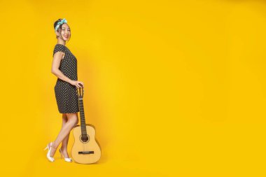 Pin tarzı giyinmiş güzel Asyalı kız parlak sarı bir arka planda gitarıyla. İzole edilmiş. Boşluğu kopyala