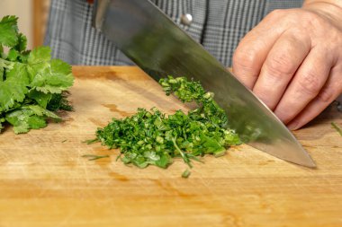 Mutfak tahtasındaki kadın aşçı salata için yeşillik kesiyor. Yakın plan.