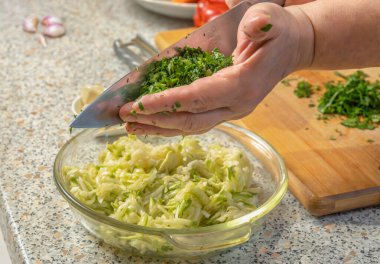 Aşçı, krep yapmak için rendelenmiş kabaklı bir tabağa ince doğranmış yeşillikler ekler. Yakın plan.
