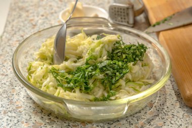 Şef, cam bir tabakta kaşıkla krep yapmak için kabak hamuruyla ince doğranmış sebzeleri rendeleyip rendeleyecek. Yakın plan.