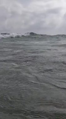 Deniz dalgası sahile doğru yuvarlanıyor ve kamerayı su basıyor.