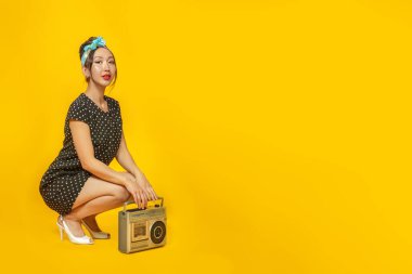 Pin tarzı giyinmiş güzel bir Asyalı kız. Parlak sarı arka planda geçmişe dönük kayıt cihazı var. İzole edilmiş. Boşluğu kopyala