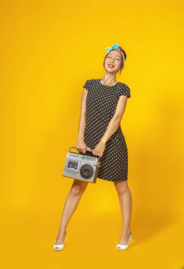 Pin tarzı giyinmiş güzel bir Asyalı kız. Parlak sarı arka planda geçmişe dönük kayıt cihazı var. İzole edilmiş